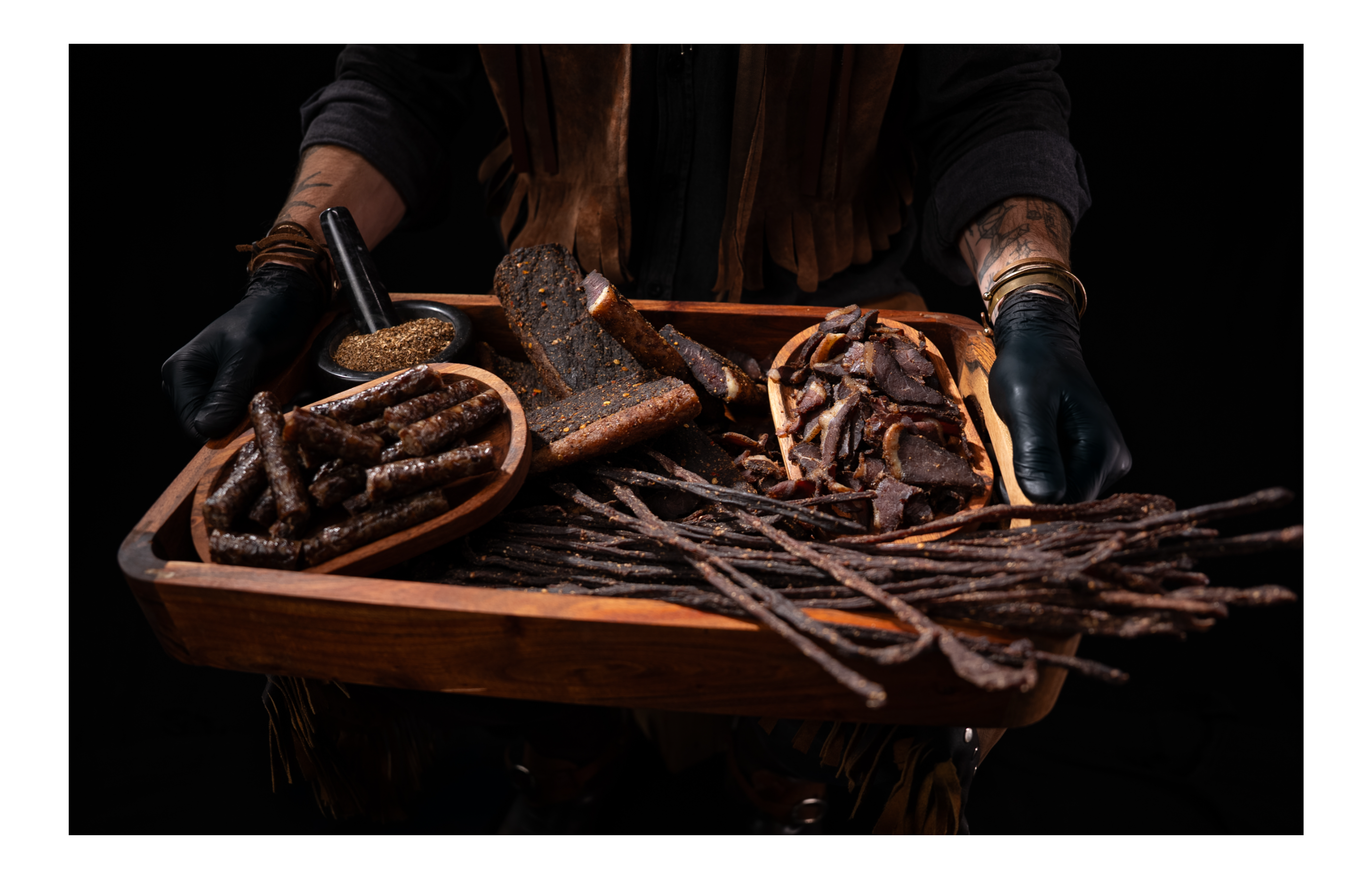 Hand presenting premium free-range sliced biltong, snapsticks and droëwors on a wooden serving tray