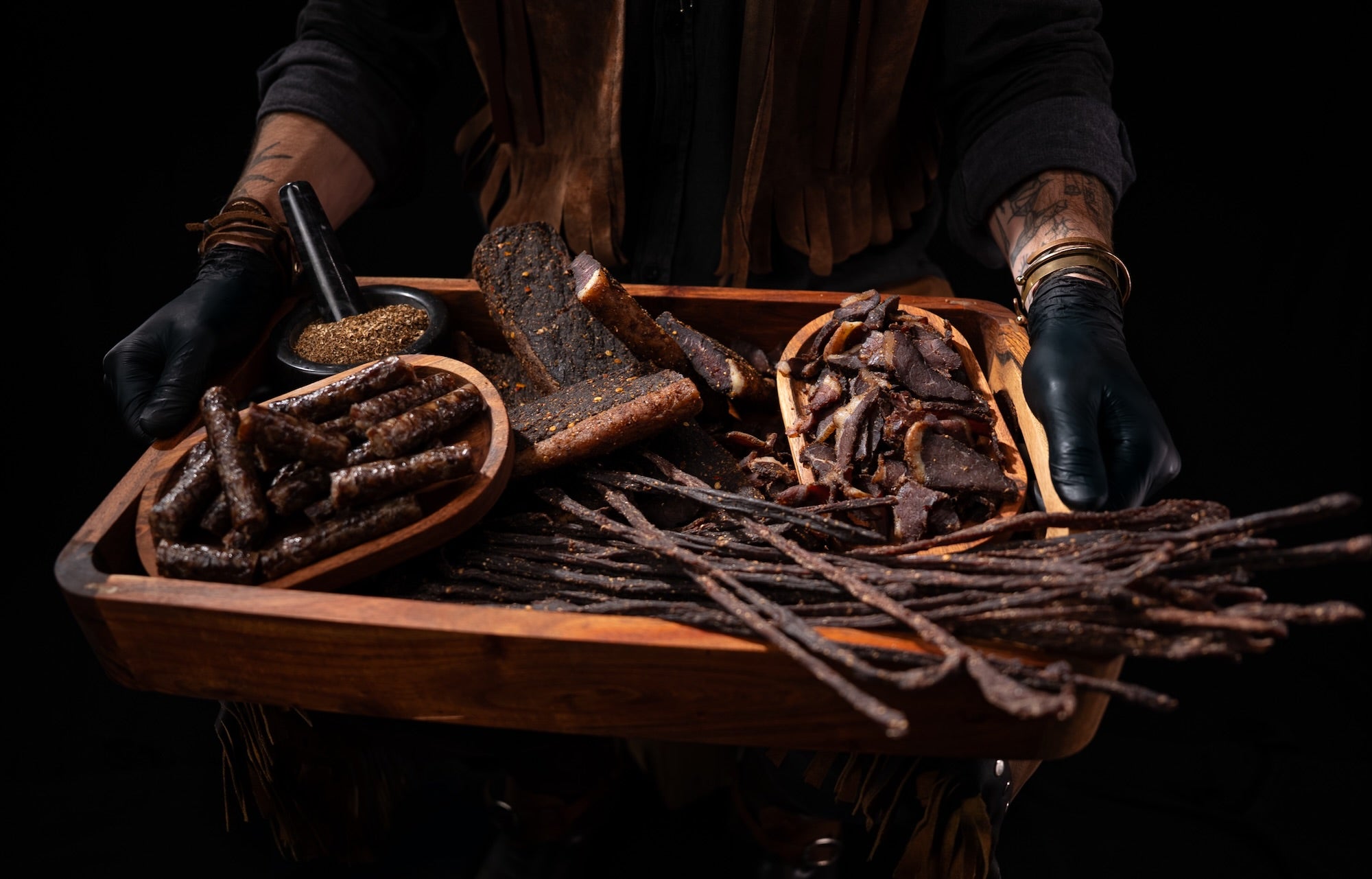 Hand presenting premium free-range sliced biltong, snapsticks and droëwors on a wooden serving tray
